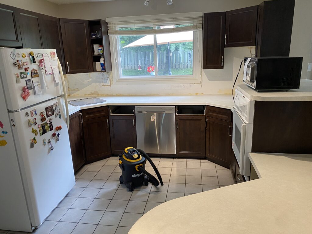 Modern kitchen with dark cabinets, light countertops, and a central vacuum cleaner.